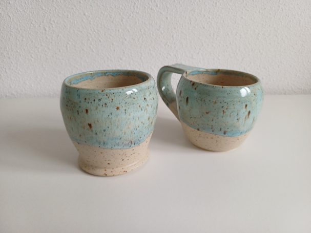 Twee keramische mokken met een blauwgroene glazuur en een beige onderkant.