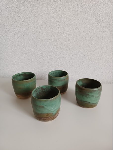 Vier geglazuurde keramische kopjes in groene en bruine tinten.