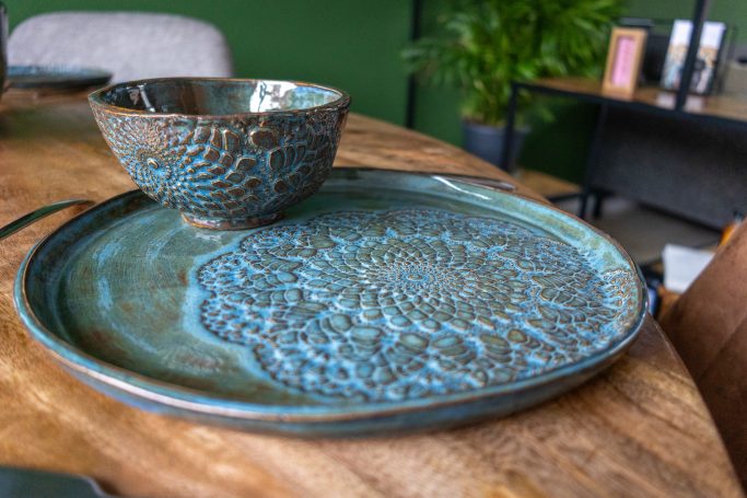 Een gedetailleerd, turquoise bord met een bijpassende kom op een houten tafel.