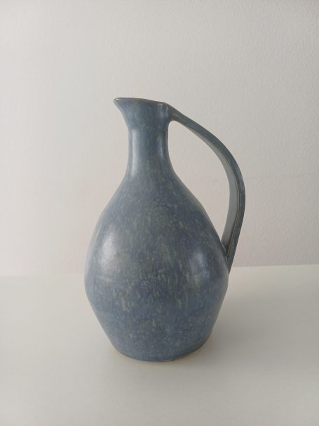 Blauw keramisch kruikje met een gebogen handvat en ronde basis.