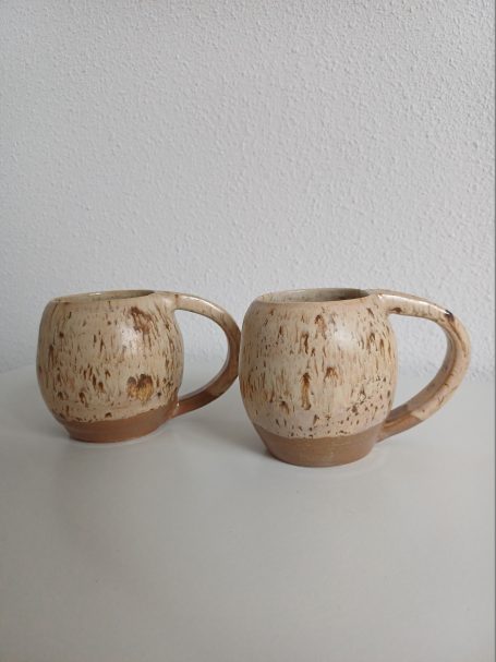 Twee aardewerk mokken met een geraffineerde, lichte kleur en een stevige handgreep.
