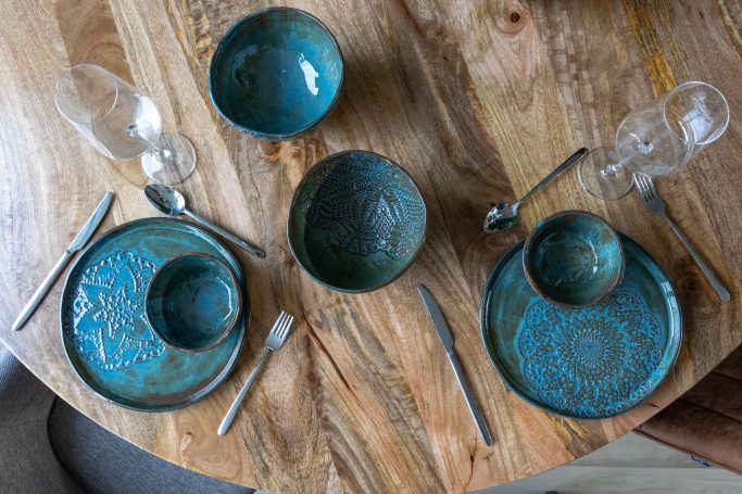 De tafel is gedekt met turquoise borden, glazen en bestek op een houten tafel.