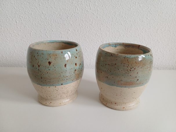 Twee keramische mokken met een lichtblauwe rand en een beige onderkant.