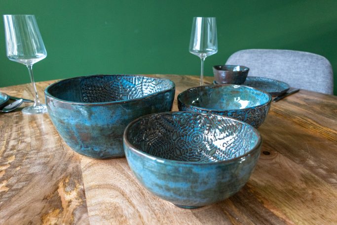 Drie aardewerken kommen in verschillende maten met een turquoise glazuur op een houten tafel.